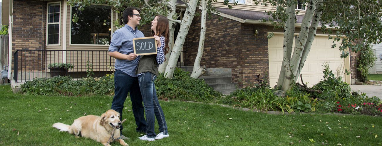 a couple with dog holding a sold sign